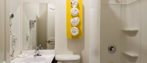 A bathroom with a white sink, toilet, and shower. There is a yellow towel rack with three towels.