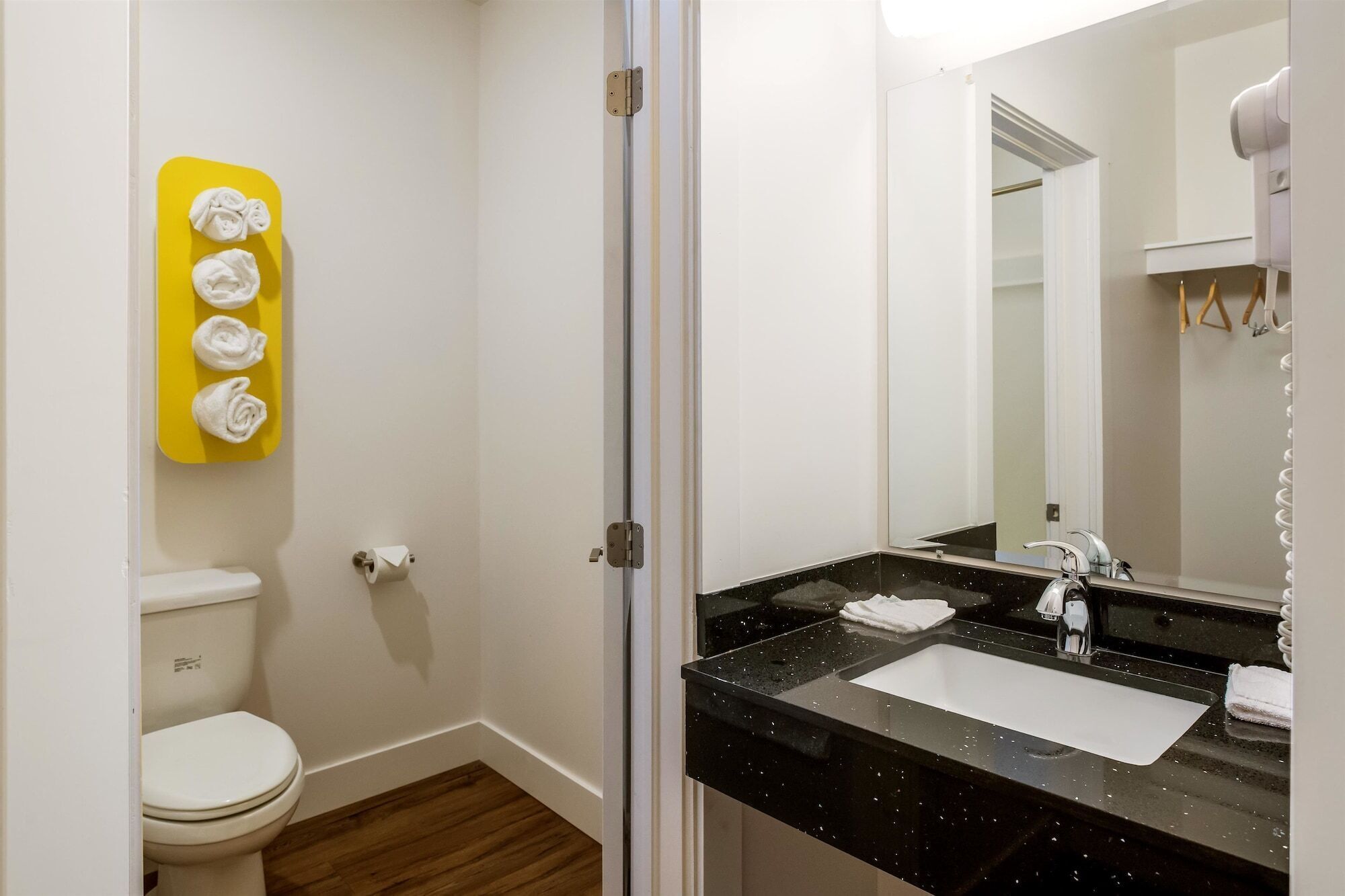 A bathroom with a toilet, a sink with a mirror, and a yellow towel rack.