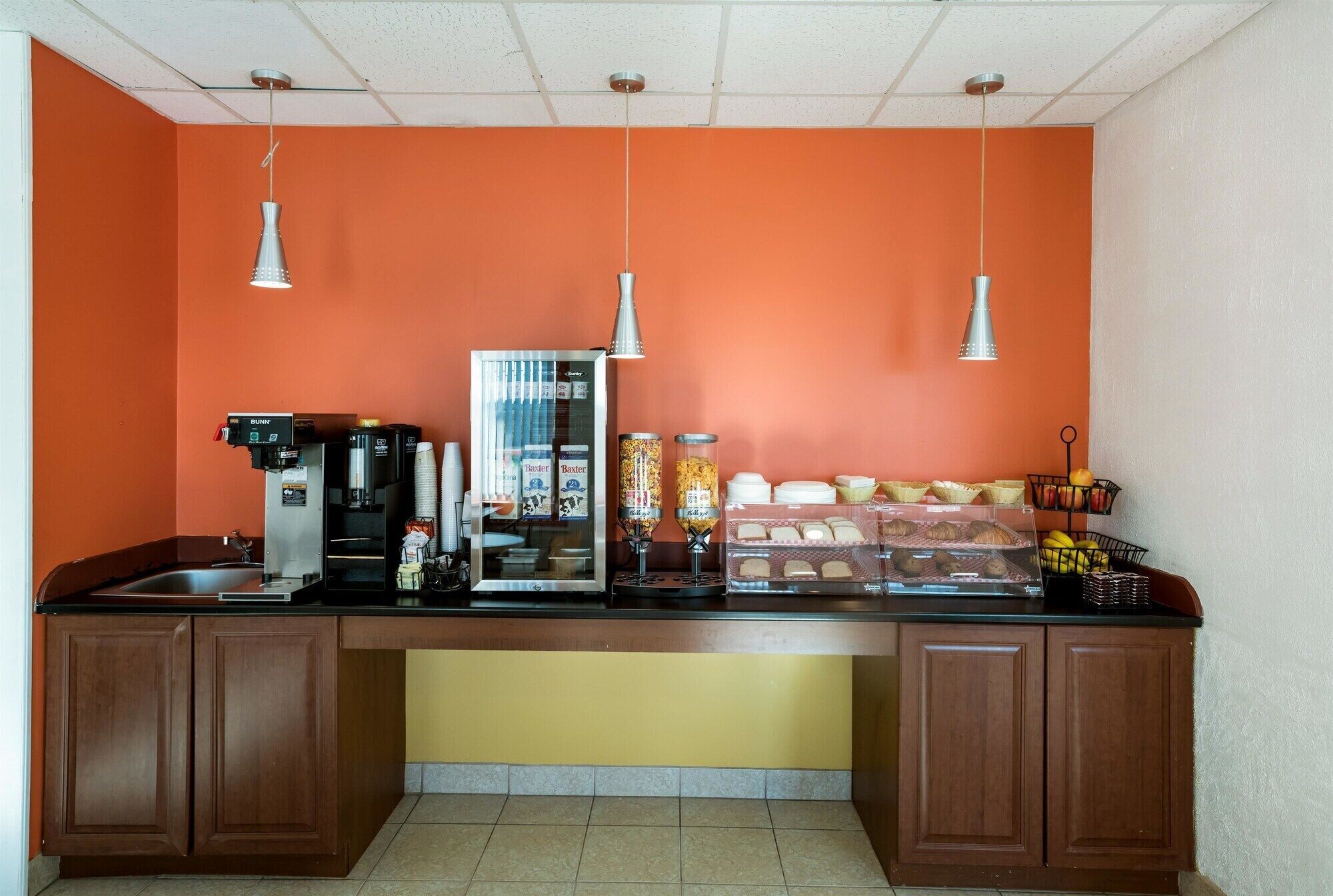A kitchenette with a coffee machine, a refrigerator, and a glass display case with food items.