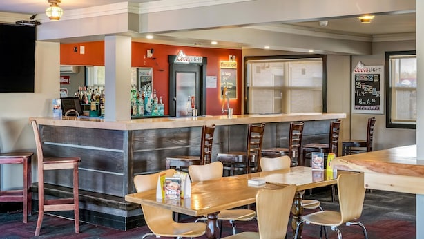 Zona de bar con taburetes y mesas, una barra con un cartel que dice "Coors Light" y un panel con la oferta de pizza y carne.