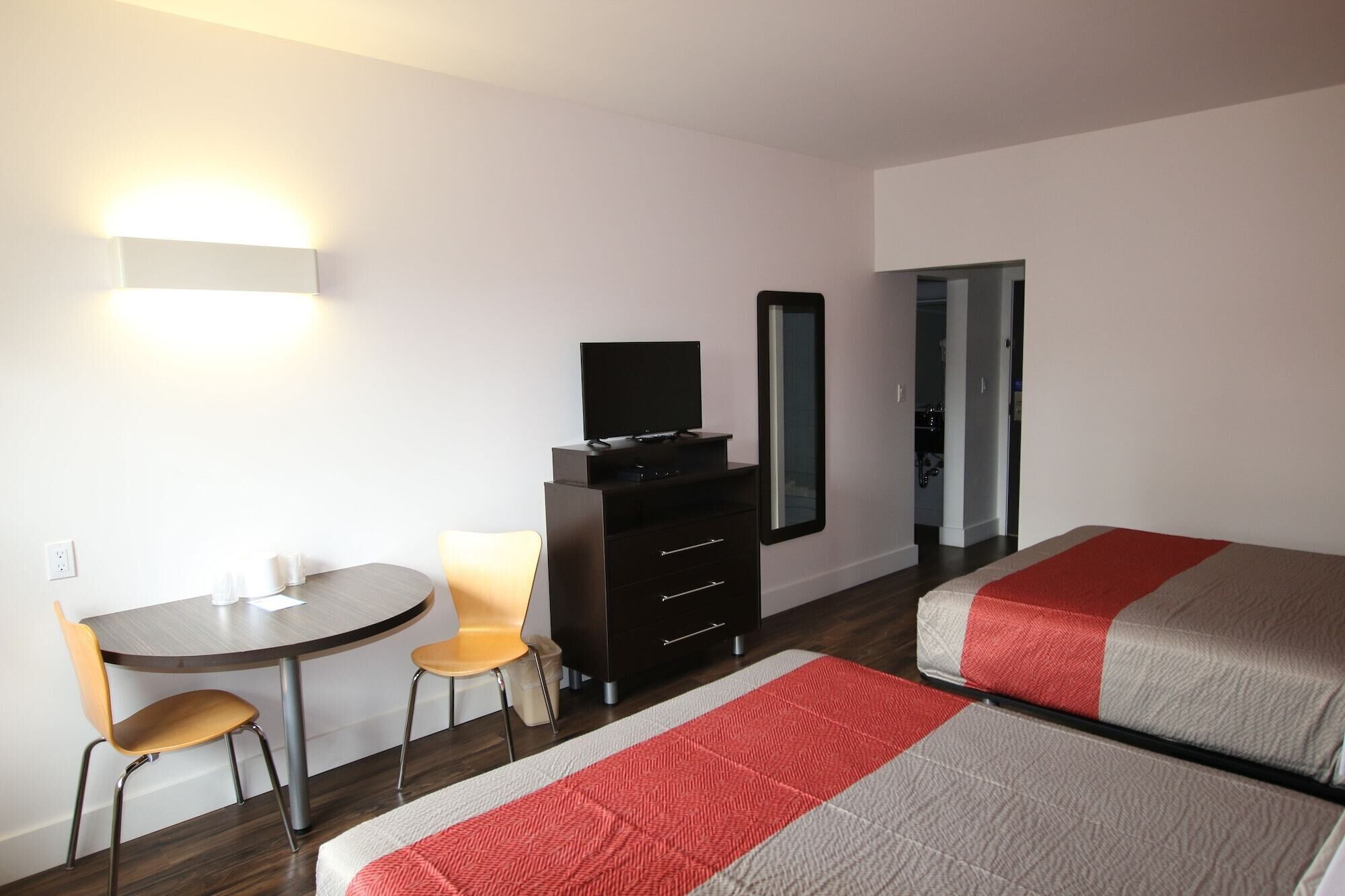 Habitació d'hotel amb un llit, una taula de nit, una cadira, un armari, un televisor i un mirall.