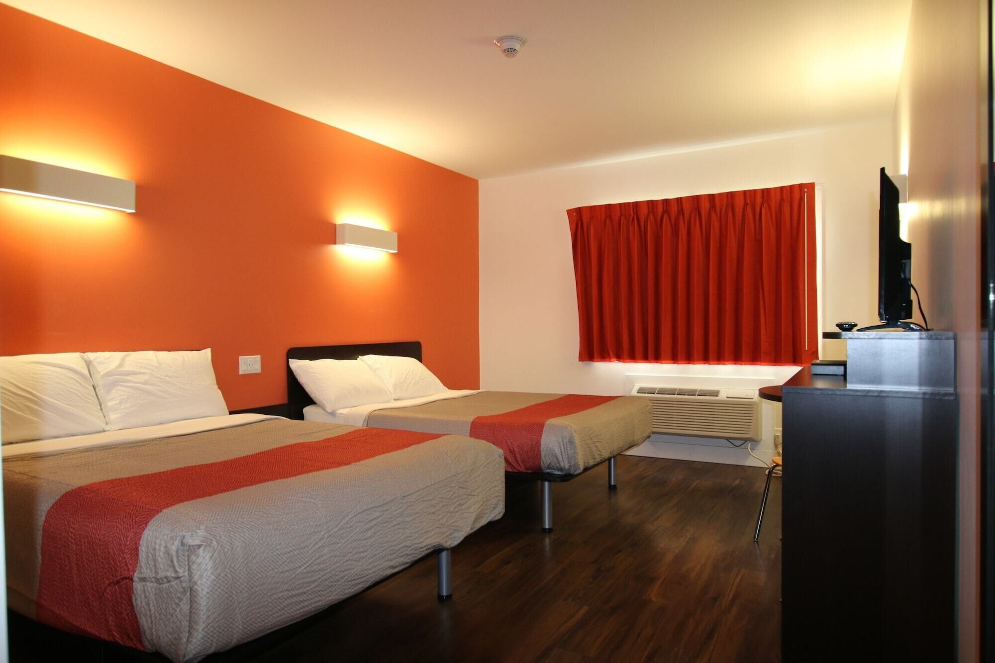 Una habitación de hotel con dos camas, un televisor y una ventana con cortinas rojas.