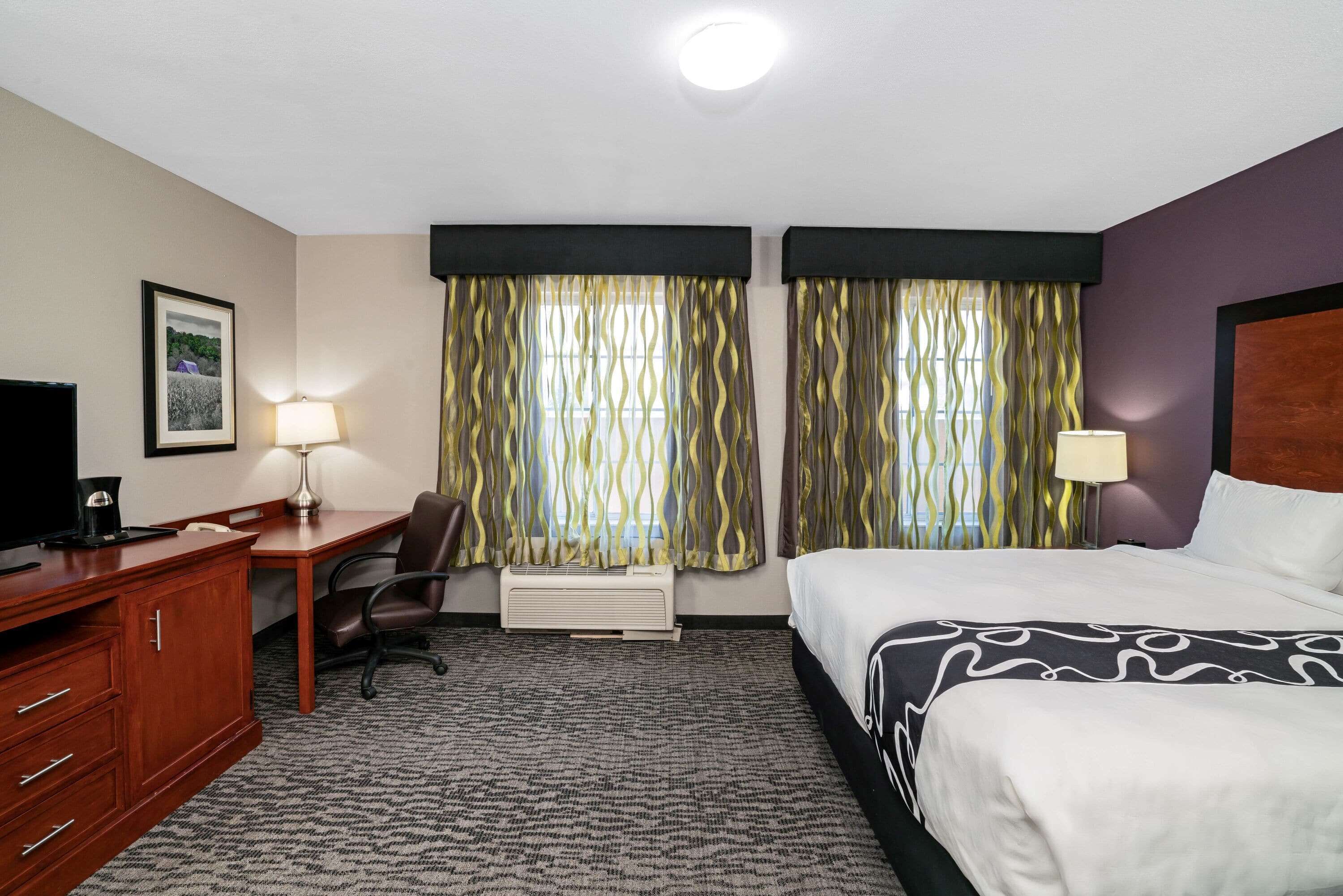 A hotel room with a bed, desk, chair, and a TV.