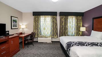 A hotel room with a bed, desk, chair, and a TV.