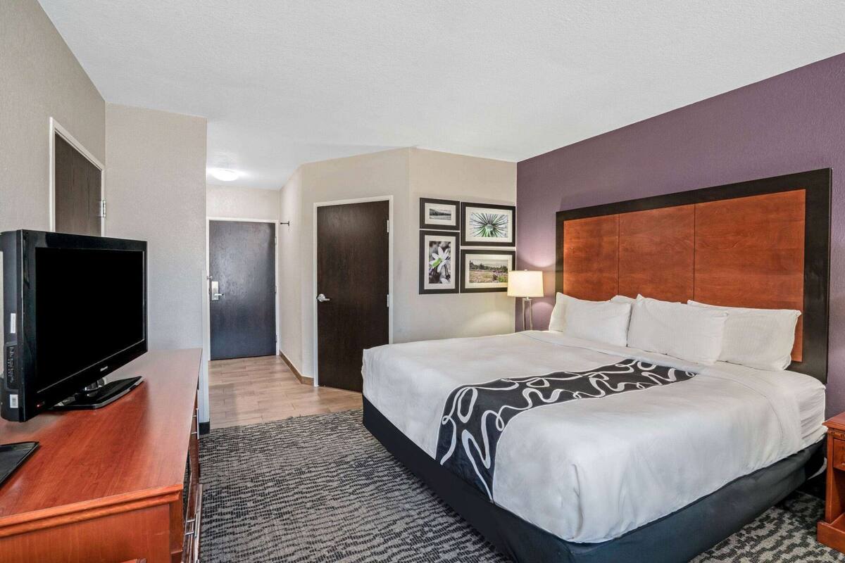 Une chambre d’hôtel avec un lit, un téléviseur posé sur une commode en bois et une porte donnant sur une autre pièce.