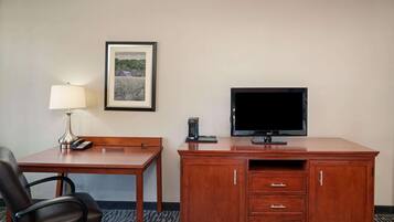A hotel room with a wooden desk, a chair, a television, a lamp, and a framed picture on the wall.