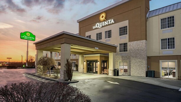 La Quinta Inn & Suites -hotellin rakennus, jossa on katettu sisäänkäynti, pysäköintialue ja taivaalla auringonlasku.
