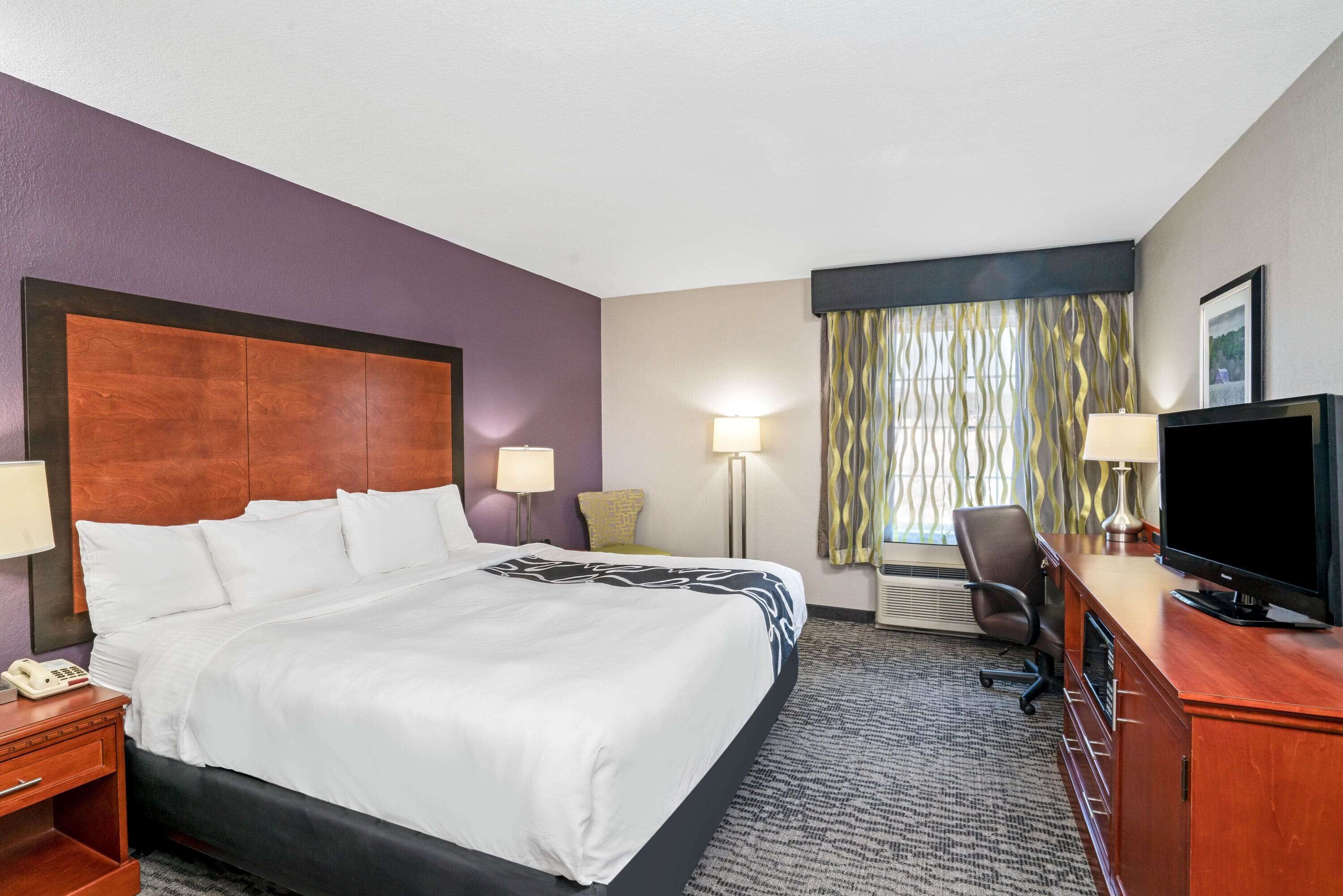 A hotel room with a large bed, bedside lamps, a desk with a television, and a window with curtains.