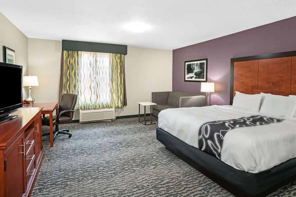 Une chambre d’hôtel avec un lit, un bureau avec une télévision, une chaise et une petite table.