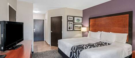 A hotel room with a bed, a TV on a wooden stand, and framed pictures on the wall.