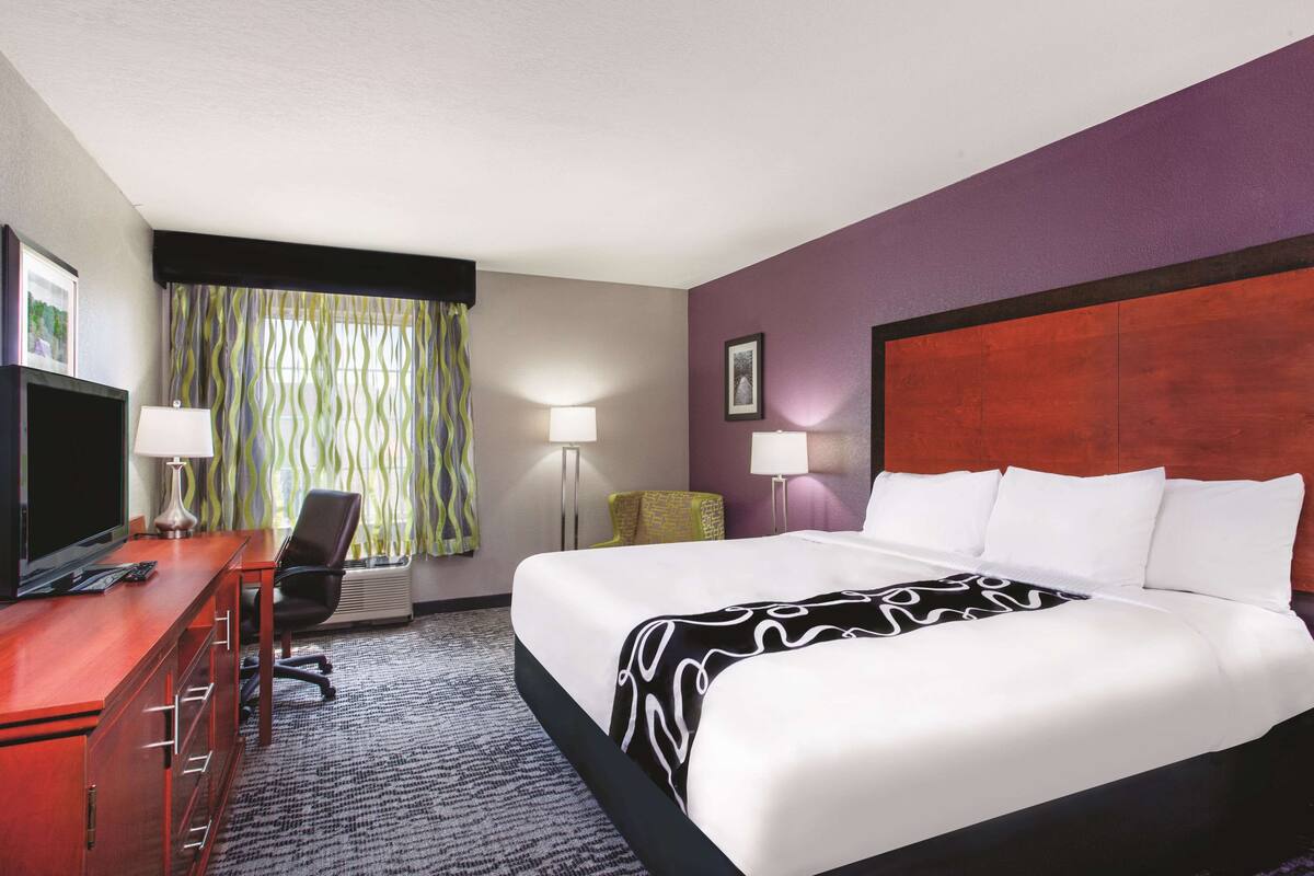 Une chambre d’hôtel avec un grand lit, un bureau avec un ordinateur, une chaise et deux lampes.