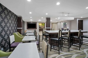 Une salle à manger d’hôtel avec des tables et des chaises, un téléviseur et une cuisine en arrière-plan.