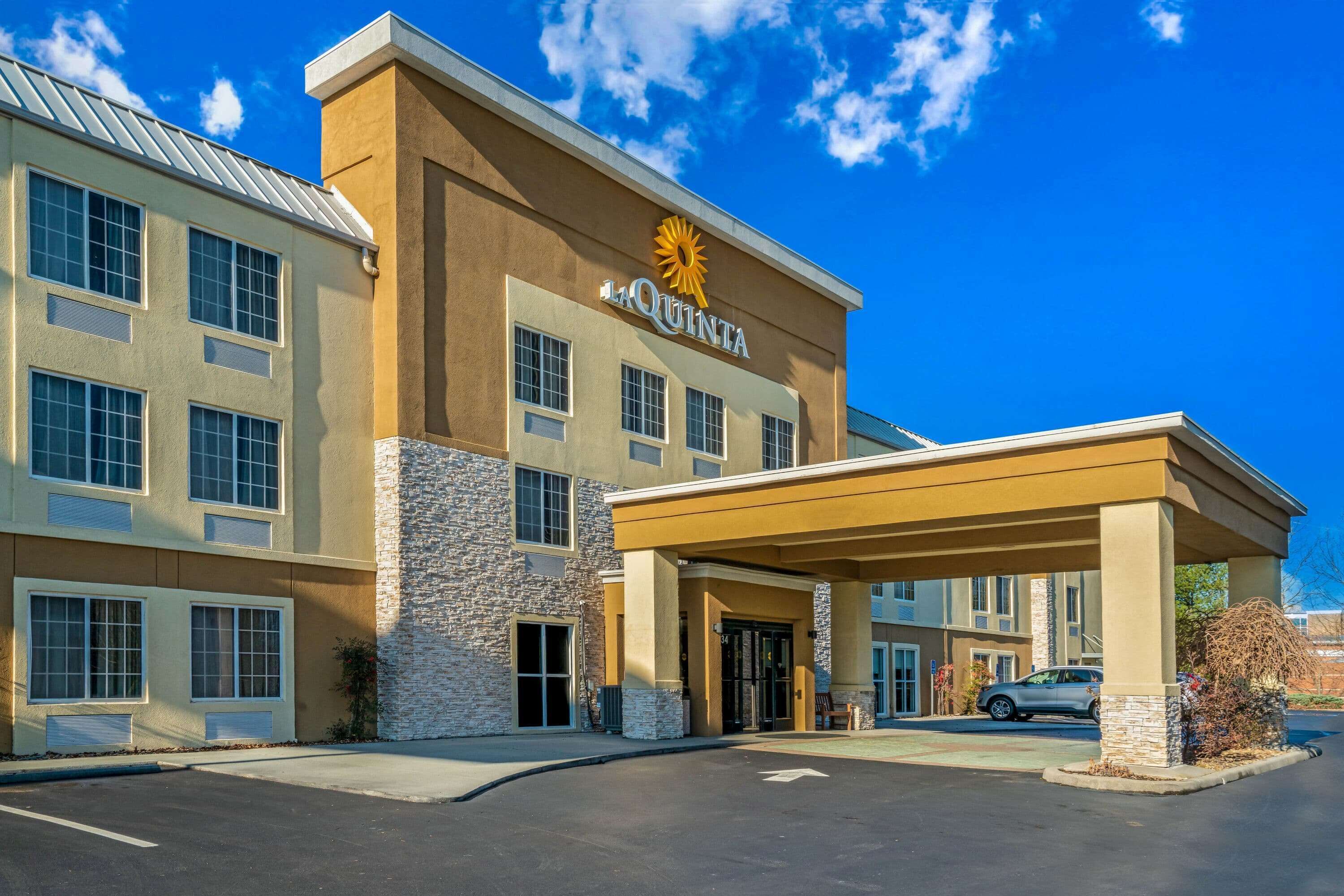 A hotel with a stone facade, a covered entrance, and a parking lot.