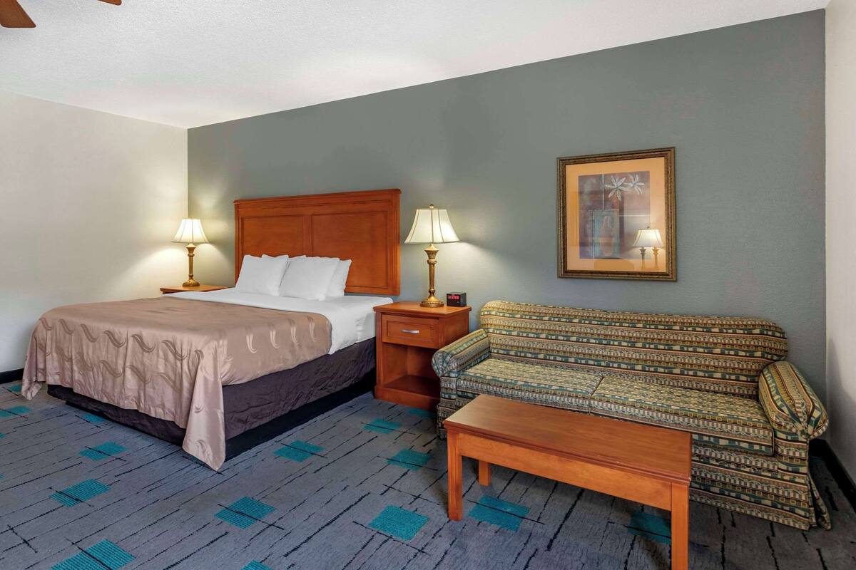 A hotel room with a bed, a sofa, a nightstand, and a lamp.