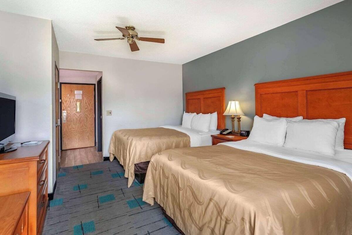 A hotel room with two beds, a wooden dresser, a ceiling fan, and a television.