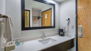 Un baño de hotel con un lavamanos blanco, un espejo, un perchero para toallas, un secador de pelo y una cafetera.