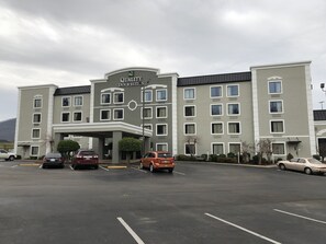 Un hotel con un diseño moderno, que destaca un letrero grande de 'Quality Inn & Suites'. Hay varios espacios de estacionamiento frente al edificio.