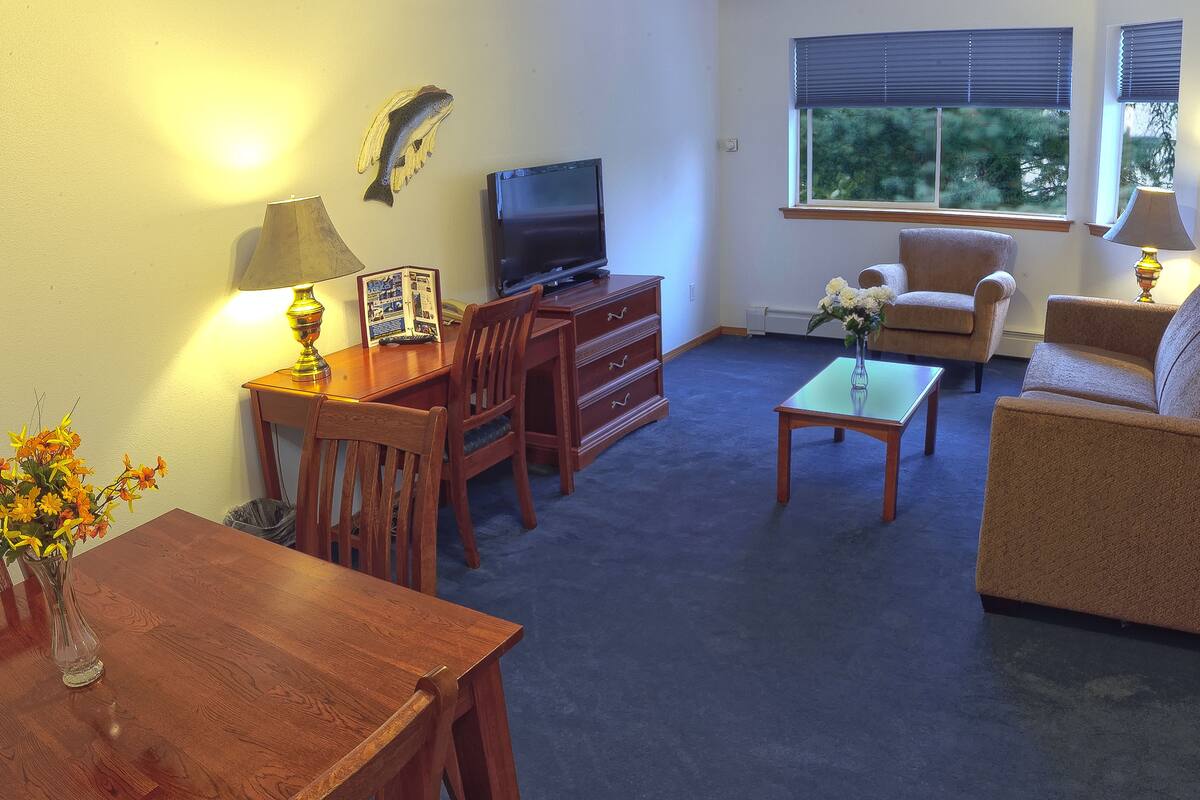 A living room with a TV, wooden furniture, a sofa, and a window with blinds.