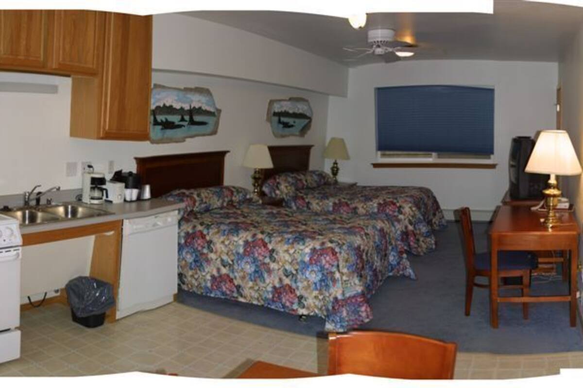 A compact kitchen with a stove, microwave, and sink, a small dining area with a table and chairs, and a bedroom with two beds and a nightstand.