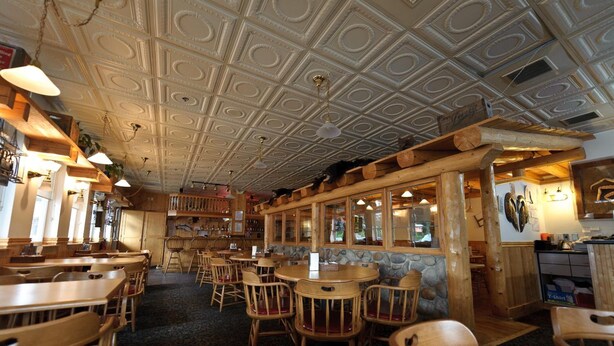 Ein Restaurantinnenraum mit Holztischen und -stühlen, einer Wand aus Stein und einer dekorativen Decke.