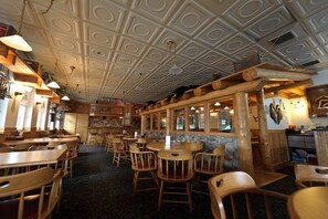 Interior de restaurante con mesas y sillas de madera, pared decorativa de piedra y techo ornamental.