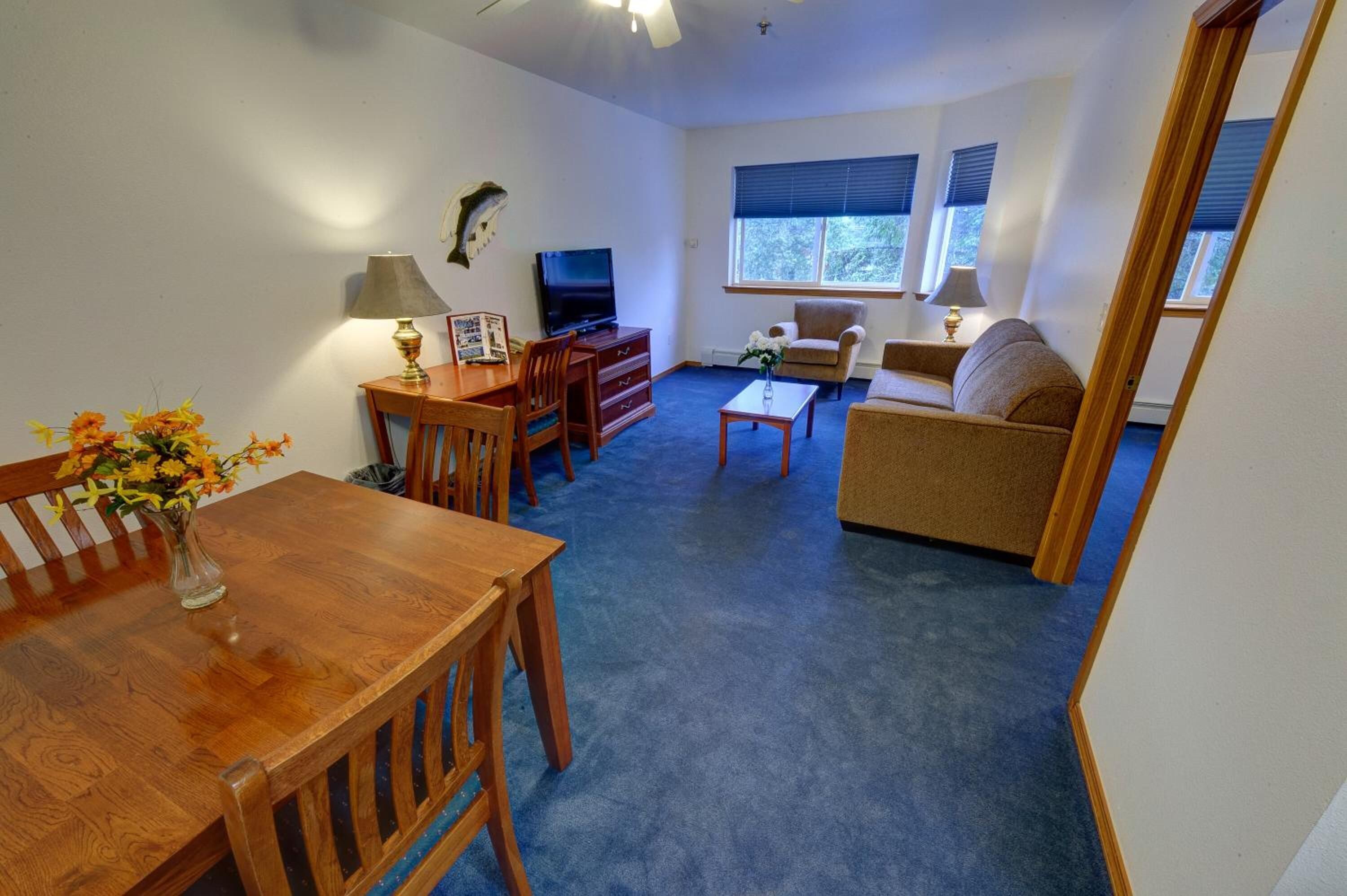 A living room with a wooden dining table, chairs, a sofa, a TV, and a window with blinds.