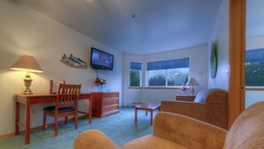 Ein Wohnzimmer mit einem Holztisch, einem an der Wand befestigten Fernseher, einer Couch und einem Fenster mit Jalousien.