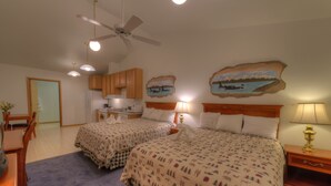 Ein Schlafzimmer mit zwei Betten, einem Deckenventilator und einer Küchenzeile im Hintergrund.