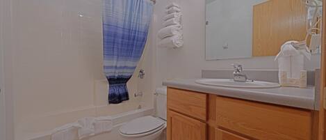 A bathroom with a bathtub, toilet, sink, and wooden cabinets.