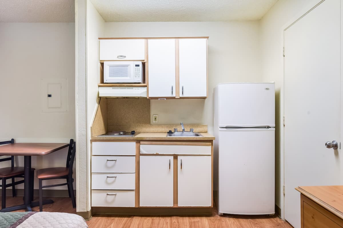Cocina compacta con gabinetes blancos, microondas, lavabo y refrigerador.
