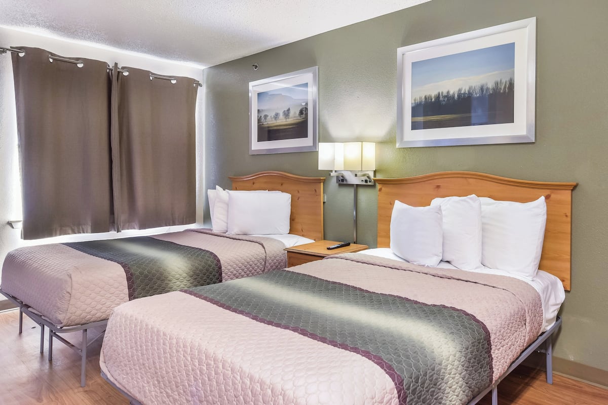A hotel room with two beds, a nightstand, a lamp, and two framed pictures on the wall.