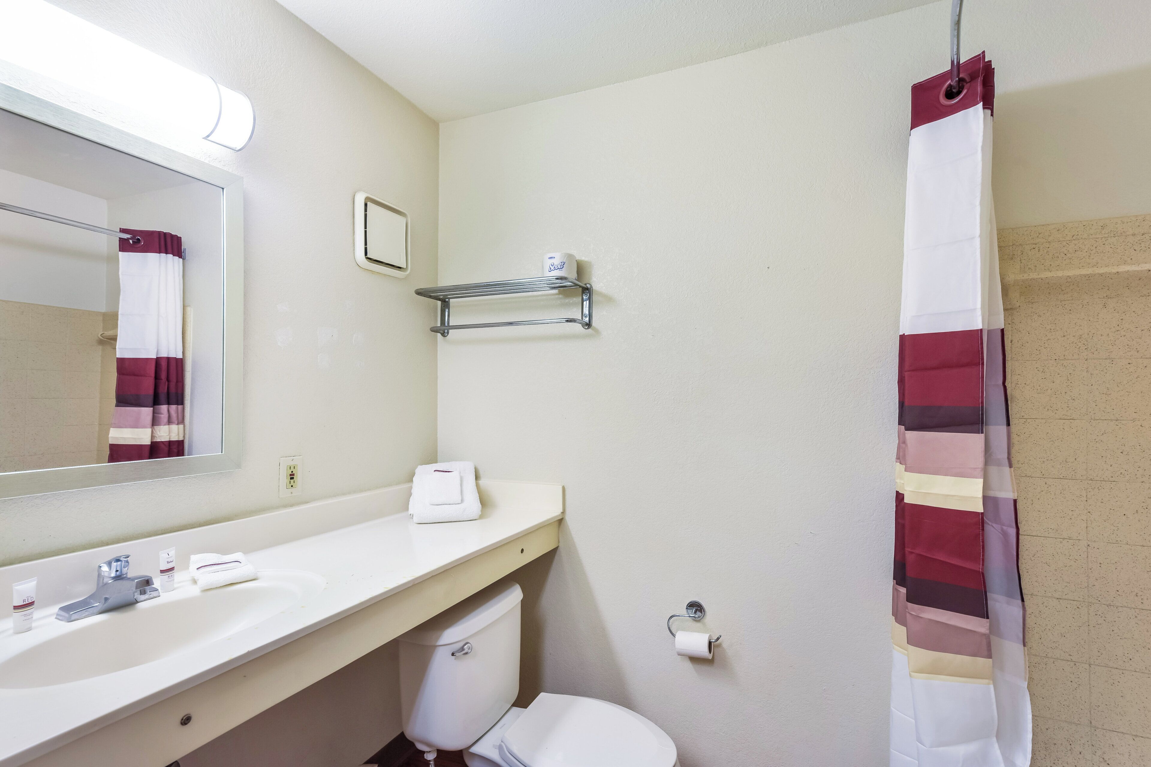 Ein Badezimmer mit weißem Waschbecken, einem Spiegel, Toilette, einer Duschvorhang und einem Handtuchhalter.