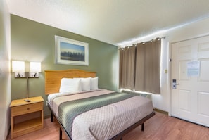 A neatly arranged hotel room with a bed, bedside lamps, a framed picture on the wall, and a door with a notice.