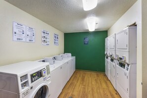 Een wasserette met meerdere wasmachines, een groene muur en instructieposters.