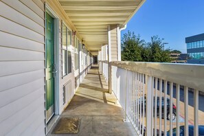 A covered outdoor corridor with a concrete floor, bordered by a railing, leading to a building entrance. - HomeTowne Studios By Red Roof Dallas - North Addison/ Tollway (Dallas)