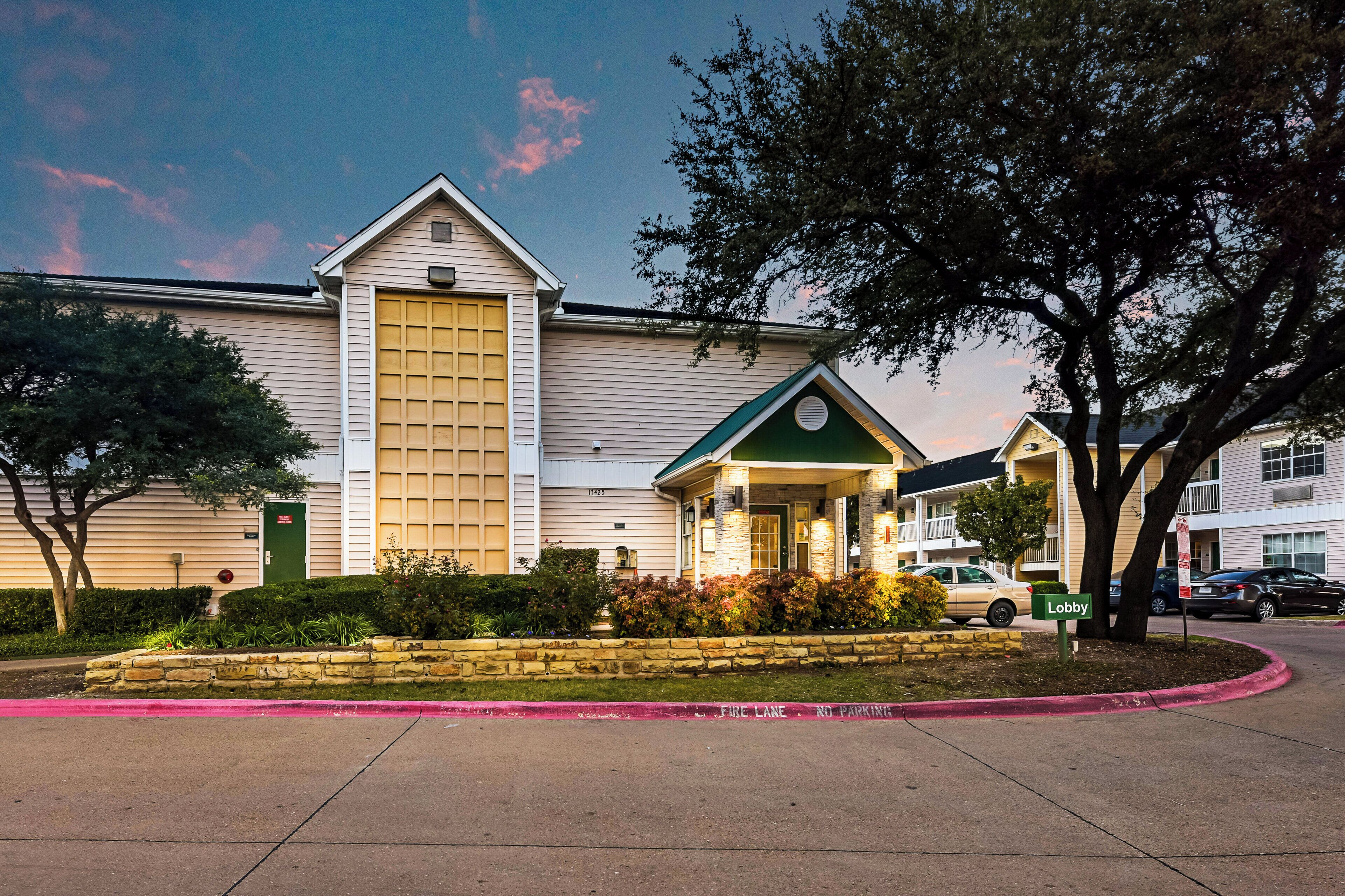 Un hotel con una entrada amplia, un toldo verde y una jardinera de piedra al frente.