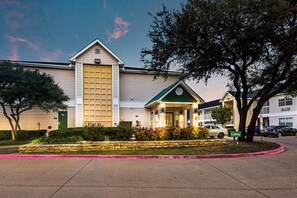 Un hotel con una entrada amplia, un toldo verde y una jardinera de piedra al frente.
