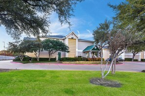 A two-story building with a green roof, a garage, and a landscaped front yard. - HomeTowne Studios By Red Roof Dallas - North Addison/ Tollway (Dallas)