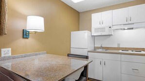 A compact kitchen with a granite countertop, white cabinets, a microwave, and a refrigerator. - Extended Stay America Suites San Diego Fashion Valley (San Diego)