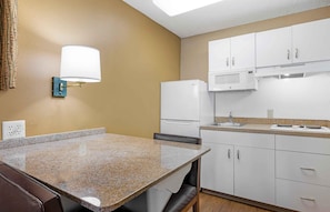 A compact kitchen with a granite countertop, white cabinets, a microwave, and a refrigerator. - Extended Stay America Suites San Diego Fashion Valley (San Diego)