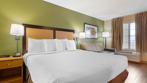 A hotel room with a large bed, two bedside tables, a nightstand, a window with curtains, and a wall-mounted air conditioning unit. - Extended Stay America Suites San Diego Fashion Valley (San Diego)
