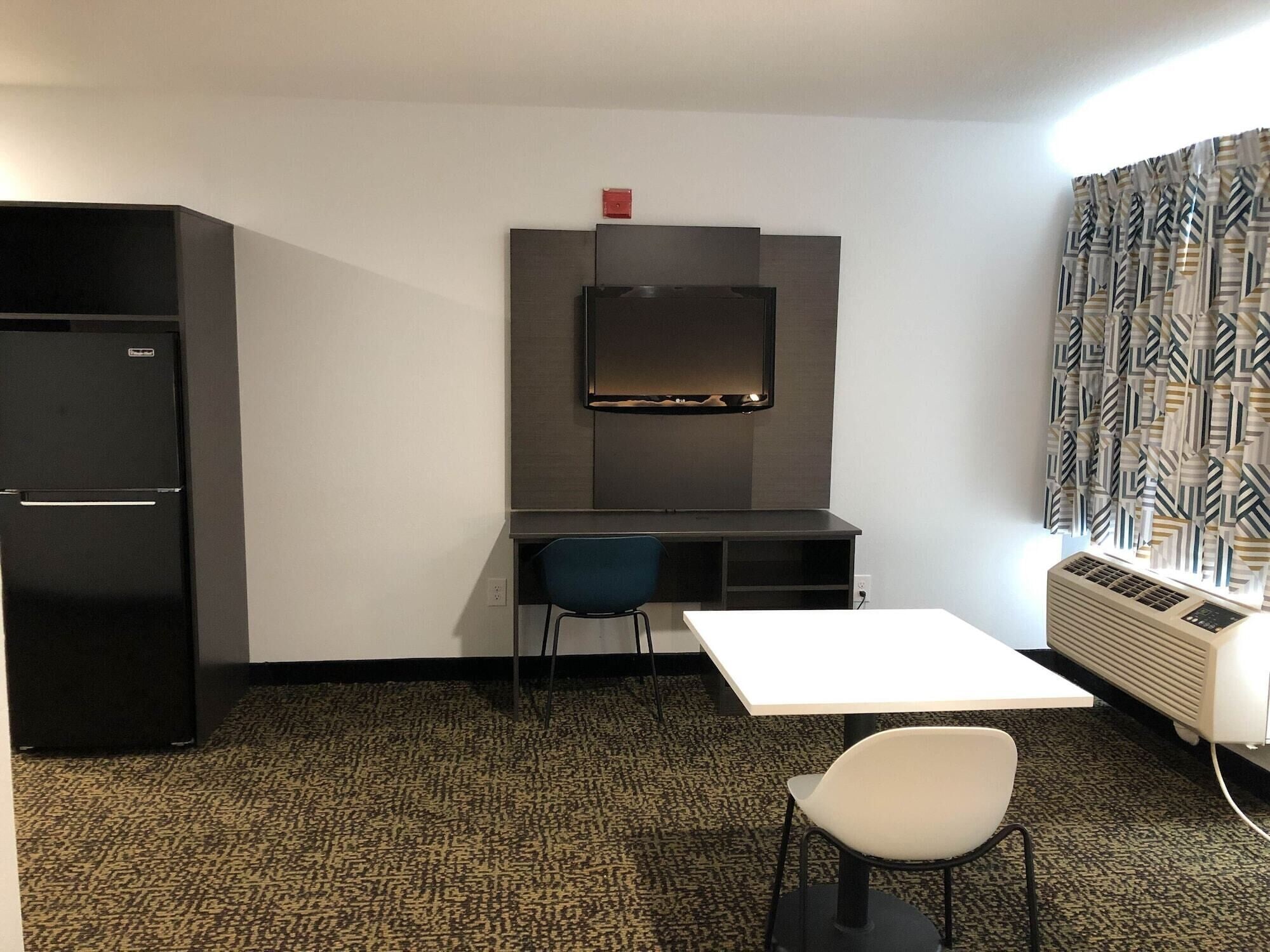 A compact room with a kitchenette, a desk, a chair, and a radiator.