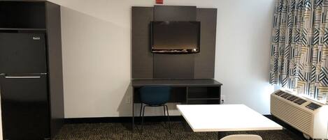 A compact room with a kitchenette, a desk, a chair, and a radiator.