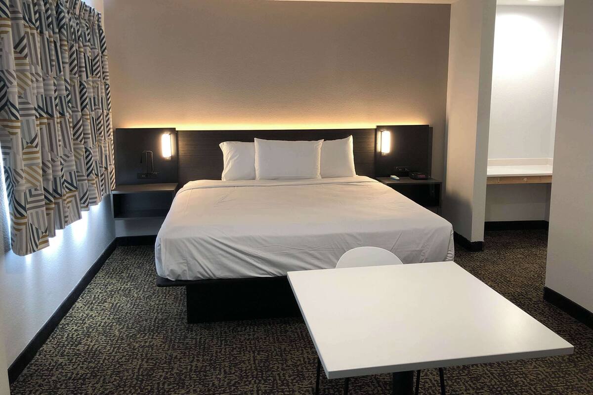 Una habitación de hotel con cama, mesitas de noche, un escritorio y una cortina estampada.