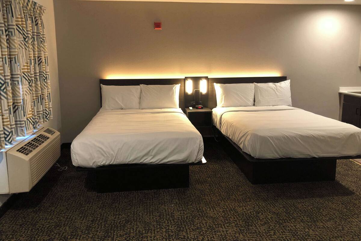 Habitación de hotel con dos camas, una mesita de noche con lámpara, un calefactor y una cortina estampada.