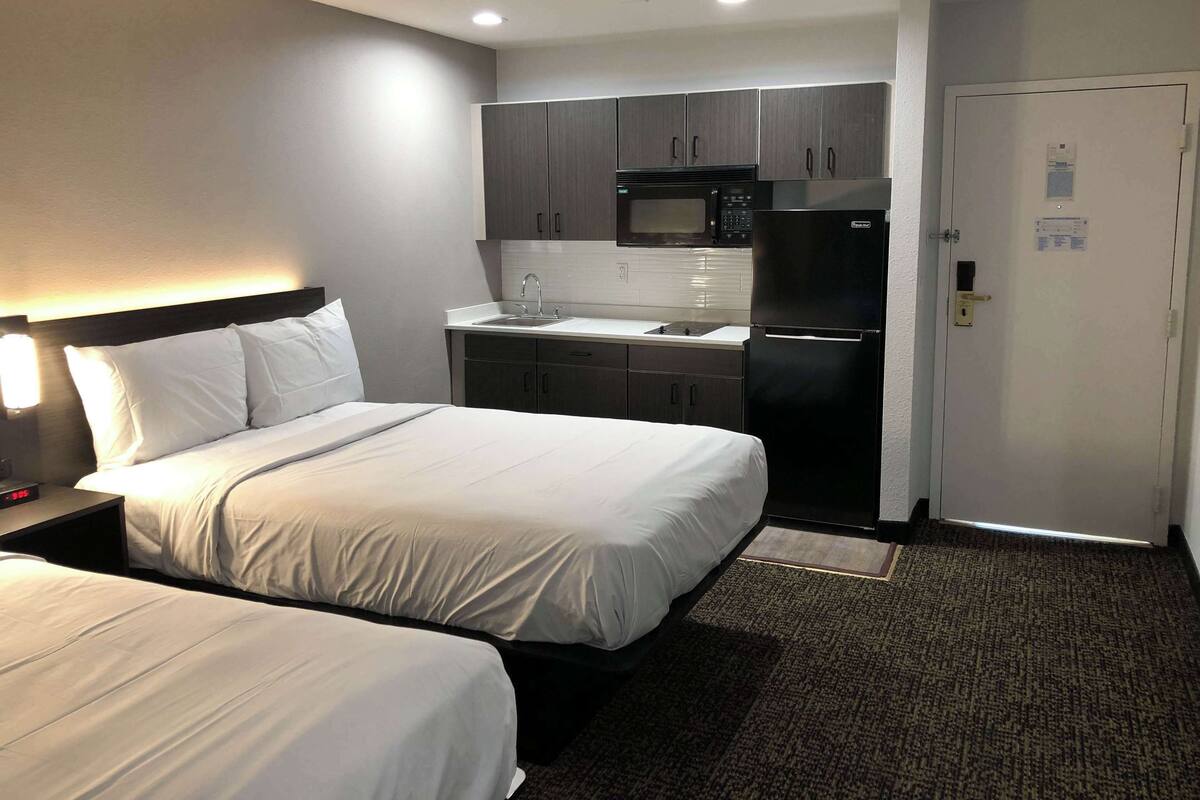 Habitación de hotel con dos camas, una kitchenette equipada con microondas, refrigerador y pileta.
