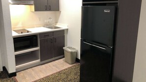 A compact kitchen with a black refrigerator, a microwave, a sink, and a trash bin. - Studio 6 Killeen, TX (Killeen)