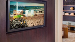 Un cuadro enmarco que muestra un hotel frente a una playa, un velero y un edificio con un cartel.