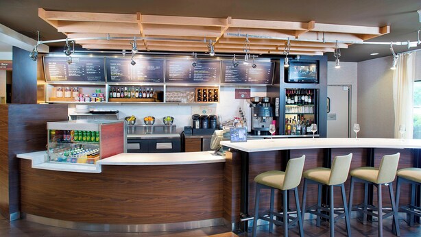 Una zona de bar moderna con mostrador de madera, taburetes y un panel con la carta.