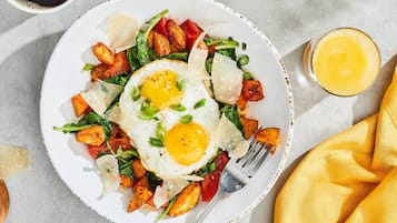 Un plato de comida con huevos, patatas y verduras, acompañado de un vaso de zumo de naranja.